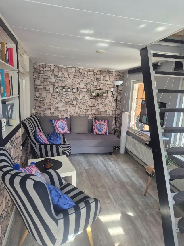 BookNoFees tatil evi: Domburg, Zeeland, Hollanda – Taş desenli duvarlı, çizgili koltuklu, gri kanepeli ve sarmal merdivenli oturma odası