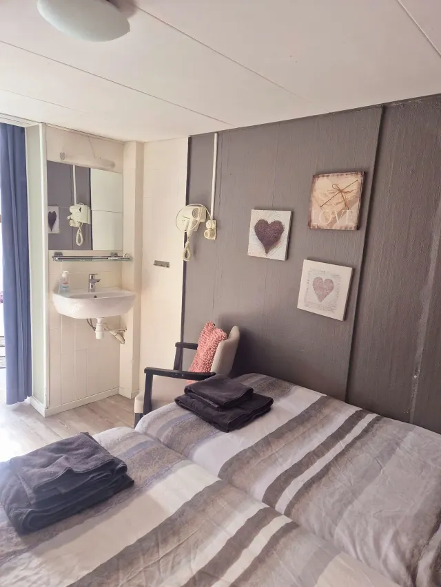 BookNoFees tatil evi: Domburg, Zeeland, Hollanda – Çizgili yatak takımları, duvar süslemeleri ve banyo içinde yer alan lavabo alanı görülebilen yatak odası
