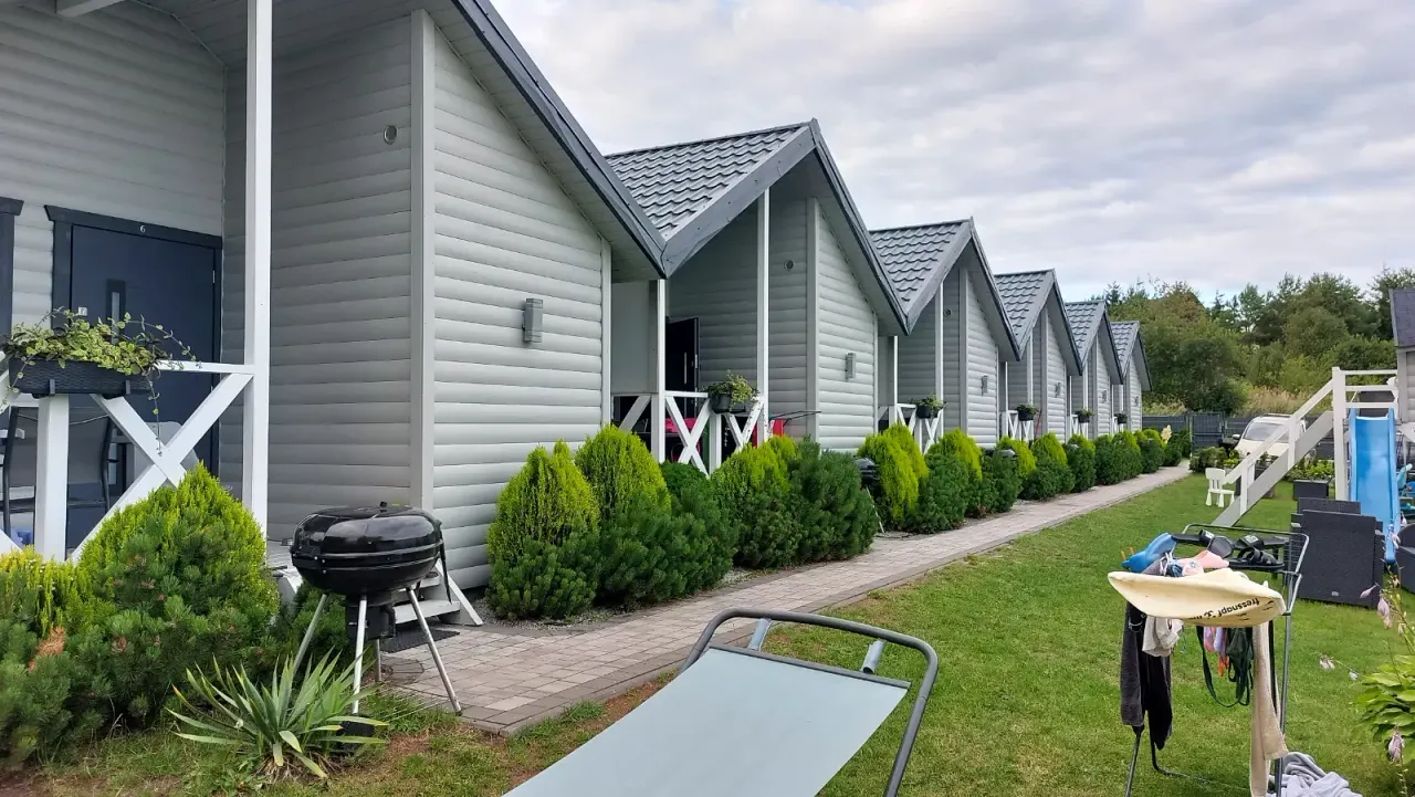 BookNoFees tatil evi: Jarosławiec, Polonya – Verandalı, barbekü ızgarası ve yeşil çim alanlı gri ahşap kulübelerden oluşan sıra